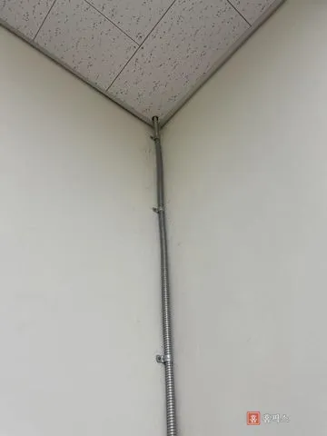 벽 모서리를 따라 새들로 고정한 가요전선관과 천장 마감부