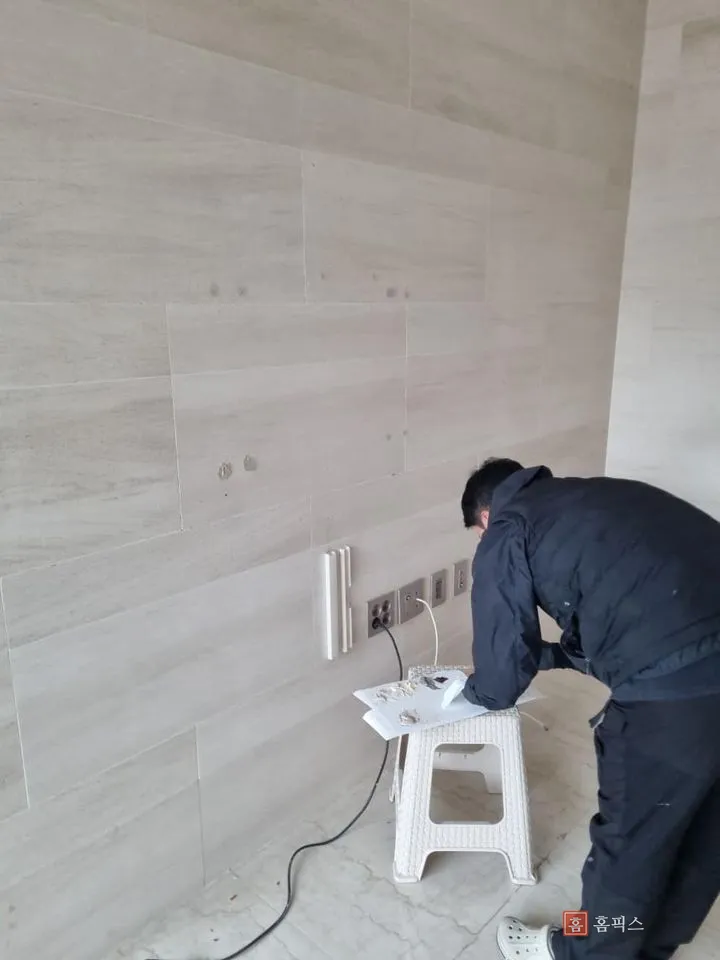 벽 앞에서 종이 위에 퍼티를 올려 조색 중인 작업자