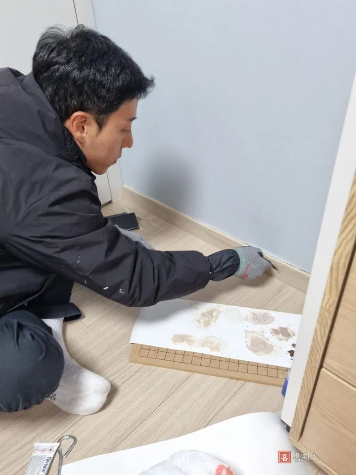 작업자가 무릎을 꿇고 몰딩 깨진 자리에 퍼티를 채우는 모습